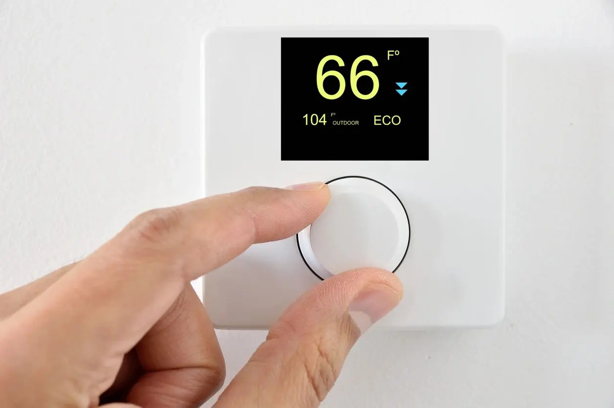 A person is adjusting the temperature on an electronic thermostat.